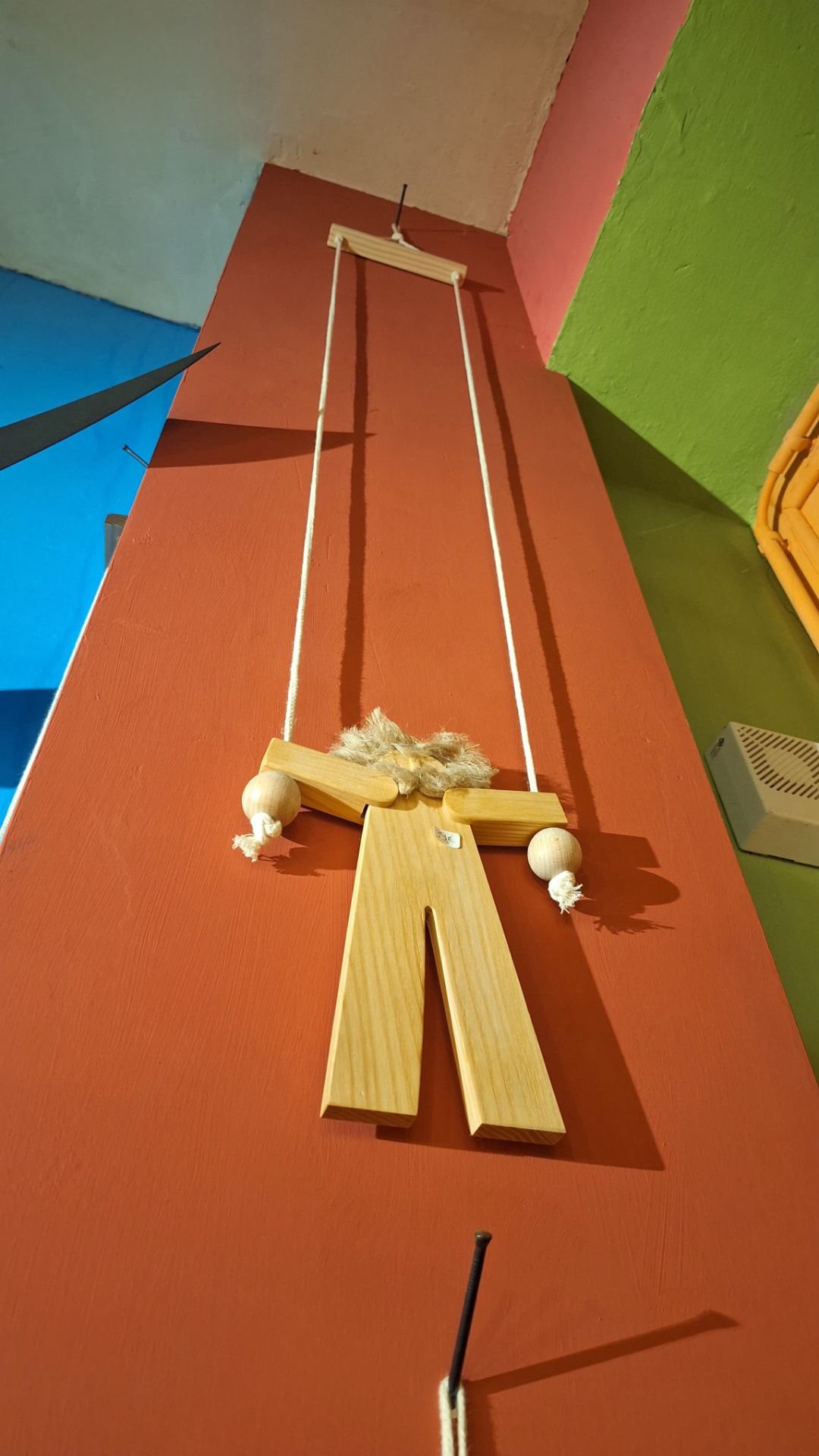 Pantin grimpeur en bois clair accroché au mur coloré de Luxiol
