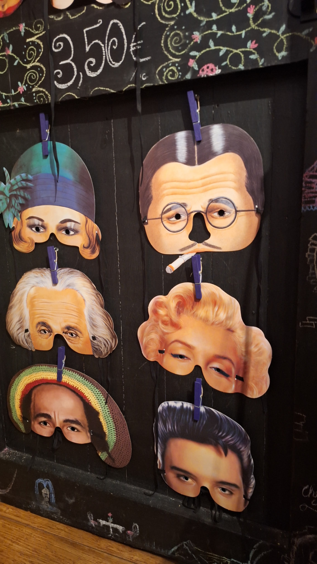 Masques de personnages célèbres suspendus à des pinces sur une porte noire chez Luxiol
