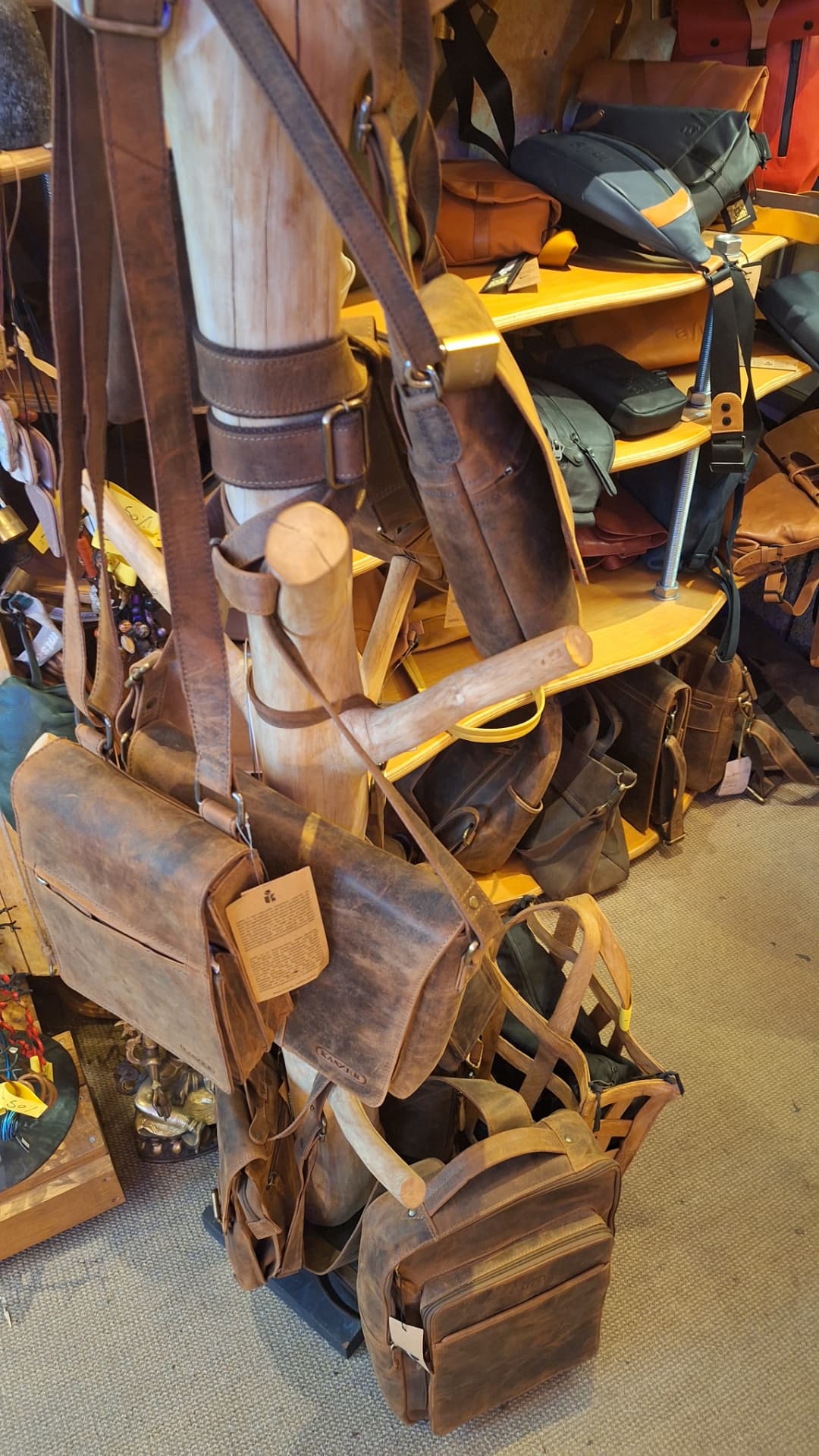 Besaces et sacs en cuir suspendus sur un présentoir en bois chez Luxiol