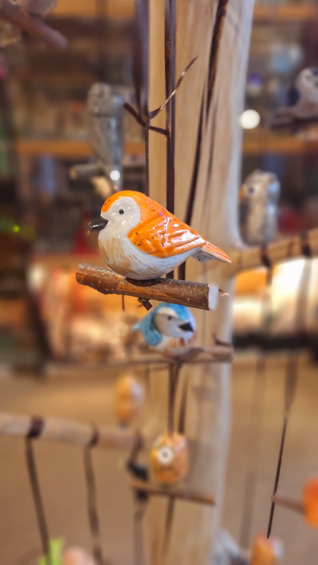 Oiseau en céramique orange et blanc posé sur une branche chez Luxiol